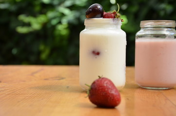 Healthy breakfast home made pudding or yogurt or granola, strawberries, cherry, honeysuckle berry, nuts and yogurt in a bowl. Vegetarian concept food.  cocktail on the background of green foliage