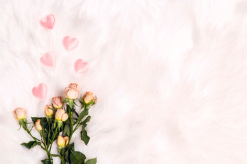 A bouquet of small roses with pink hearts on white fur background. Place for text, top down composition.