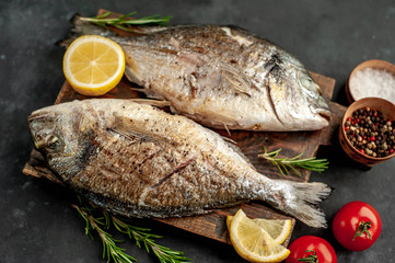 grilled dorado fish on a cutting board with spices and lemon on a stone background