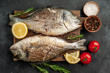 grilled dorado fish on a cutting board with spices and lemon on a stone background