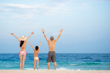 海で両手を上げる父と母と娘