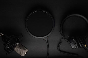 Flat lay, Studio microphone with pop filter and professional headphones. Black on a black...