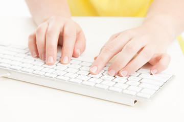 Female typing on white keyboard with yellow shirt