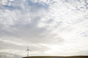a wind turbine on a hill with setting sun behind