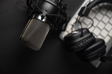 Microphone for podcasts and studio headphones on a PC keyboard on a black background, horizontal...
