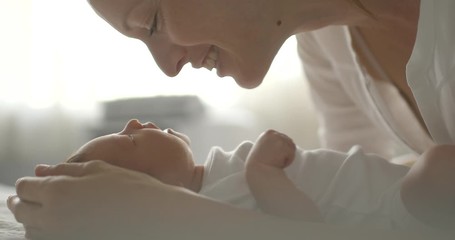 Mother and her newborn baby girl kissing, talking to her in bright bedroom setting. - Powered by Adobe