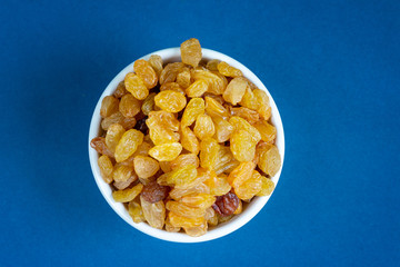 raisins in a bowl on blue background, empty space for text. Healthy organic food concept