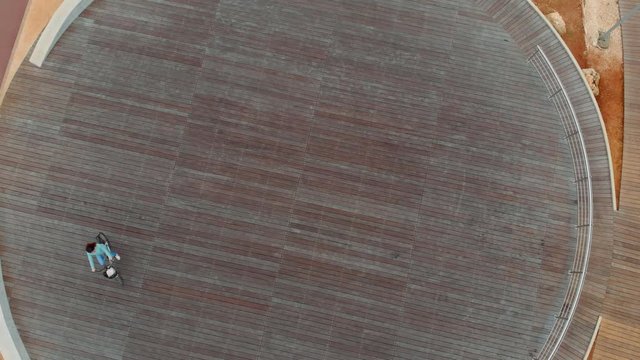 In the background, a girl rides a Bicycle on a round stadium, top view. She's wearing a blue jacket and jeans.