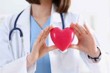 Female medicine doctor hands holding and covering red toy heart closeup. Cardio therapeutist...