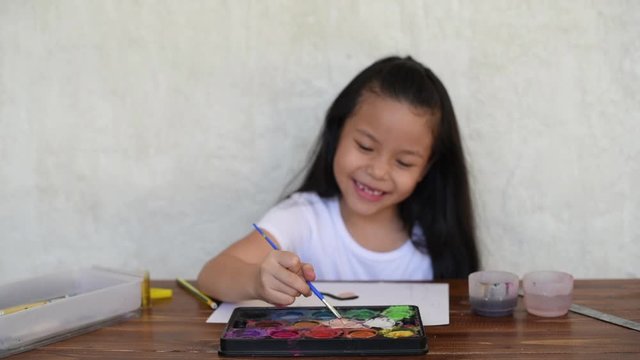 one cute little girl asian painting picture painting at easel school. education. girl drawing with crayons at the table. charming little girl painting using watercolors and gouache while sitting.