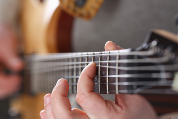 Male arms holding and playing classic shape wooden electric guitar closeup. Six stringed learning...