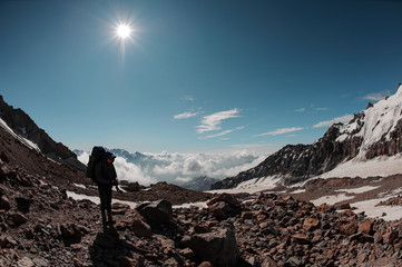 Man standing on the rocky path around the snow remnants under the sun in clear sky