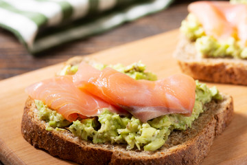 Bruschetta with avocado and salmon on a wooden Board on a brown wooden table. Toasted bread with...