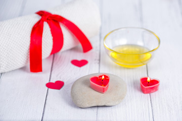 The concept of a Spa on Valentine's Day. Red heart-shaped candles, stones, massage oil and a white towel on a wooden background. Relaxation and wellness care. Bath procedure.