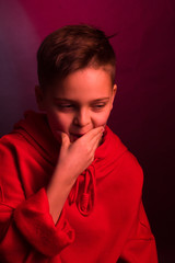 Studio portrait of a dark-haired boy, on a maroon background, in a red hoodie jacket