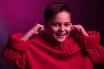 Studio portrait of a dark-haired boy, on a maroon background, in a red hoodie jacket