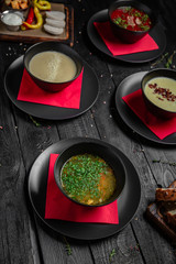 Set of different soups. Chicken broth, red borsch, lentil with bacon, mushroom cream soup. Delicious fragrant first courses. Festive table with delicious food on black boards.