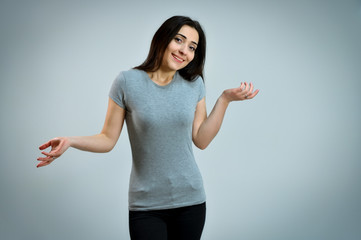 Portrait of a pretty young brunette woman in a gray t-shirt. Universal concept of a cute smiling girl on a white background. Talking, showing hands with emotions.