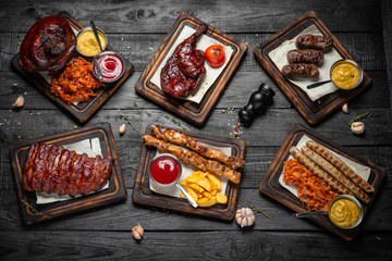Pork knuckle with crispy crust. Delicious ribs, baked duck and sausages. Octoberfest party dinner. Festive table with delicious food on black boards.