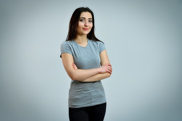 Universal concept of a cute smiling girl on a white background. Portrait of a pretty young brunette woman in a gray t-shirt. Talking, showing hands with emotions.