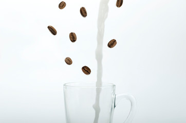 Coffee beans falling and hot milk pouring into the glass cup