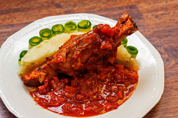 lamb shank cooked in rich tomato sauce, served with potato purée and cucumber slices 