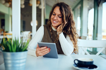 Attractive young curly brunette looking at her tablet and smiling	
