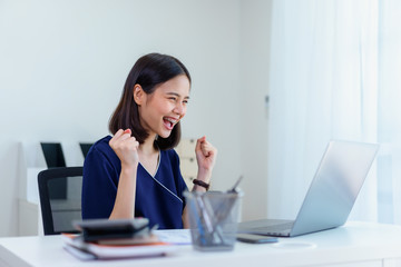 Smiling Asian woman using laptop and excited expressing winning gesture on the table in the office.