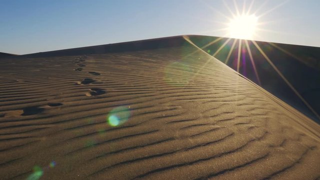 sand dunes at sunrise, walking along the sand dune in slow motion, bright sun shining in desert, dry hot scene