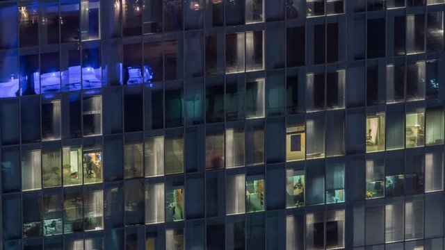 Night view of office and apartment building timelapse. High rise skyscraper with blinking windows with people moving inside. Aerial view from above. Pan down