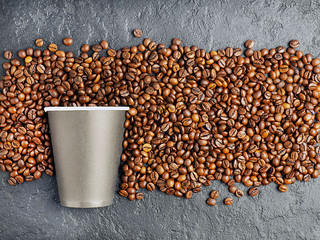Coffee beans and a paper Cup on a black concrete background.