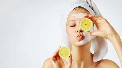 Poster Cosmetologie, huidverzorging, gezichtsbehandeling, spa en natuurlijk schoonheidsconcept. Vrouw met gezichtsmasker houdt citroenen vast. © Olesia