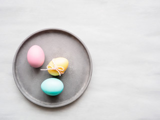 Pastellfarbige Ostereier mit einer gelben Schleife auf einem grauen Teller, Ostern, Flat lay