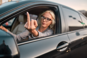 Stressed driver. Portrait of aggressive business woman showing middle finger to somebody while...