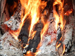 In an earthen country stove, large logs are burning in a flame.