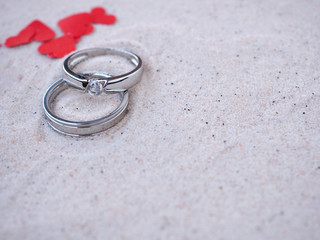 Two rings with red heart on sandy beach. Concept love