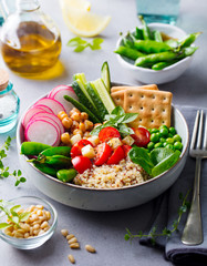 Healthy vegetarian salad. Buddha bowl. Quinoa, chickpea, tomatoes, pea, radish, cucumber, crackers. Grey stone background.