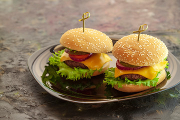 Meal, food. Two hamburger with cutlet grilled, lettuce, tomato, cheese, cucumber on a black plate.