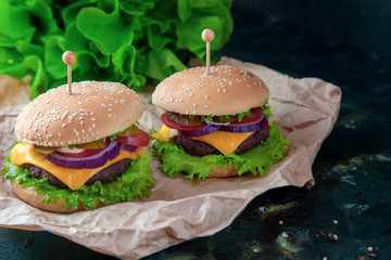 Meal, food. Two hamburger with cutlet grilled, lettuce, tomato, cheese, cucumber on a black background.