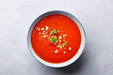 Tomato soup with fresh herbs and pine nuts in a bowl. Grey stone background. Top view.