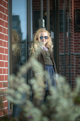 curly-haired blonde girl against the background of a brick wall and a glass window