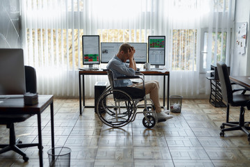 Oh no. Portrait of young upset male trader in a wheelchair holding his head in hands and feeling...