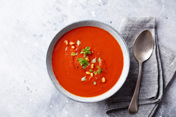 Tomato soup with fresh herbs and pine nuts in a bowl. Grey stone background. Top view.