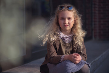 curly-haired blonde girl against the background of a brick wall and a glass window