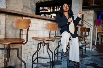 Fototapeta na wymiar Charming african american woman model in black jacket and waist bag relaxing in cafe during free time.