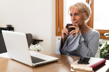 Adult woman drinking coffee watching a movie on the laptop