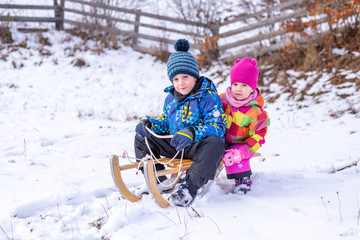 Boy and the girl are getting ready to get down from the top of the hill on a sled. Winter time .