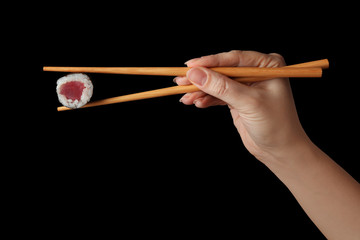 Fototapeta premium Woman holding sushi roll with chopsticks on black background, closeup