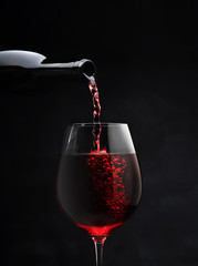 glass goblet with red wine pouring from bottle for romantic evening closeup on black background isolated