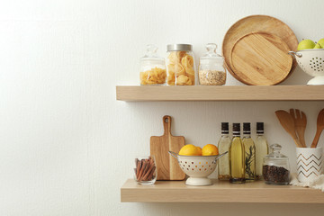 Wooden shelves with dishware and products on white wall. Kitchen interior idea
